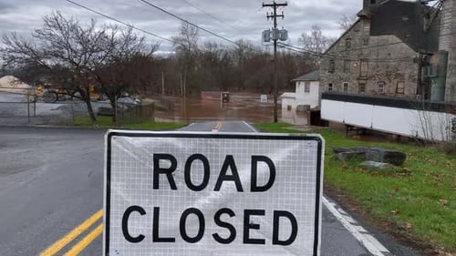 Road Closed sign in front of flooded street in USA. Aerial reveal of natural disaster with brown mur