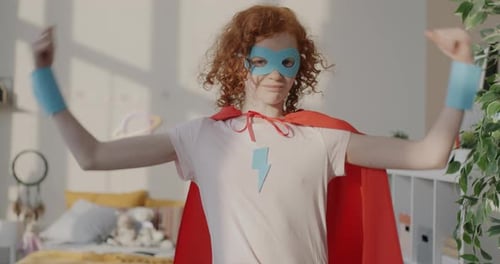 Portrait au ralenti d'une drôle de petite fille en costume de super-héros montrant les muscles du biceps souriant