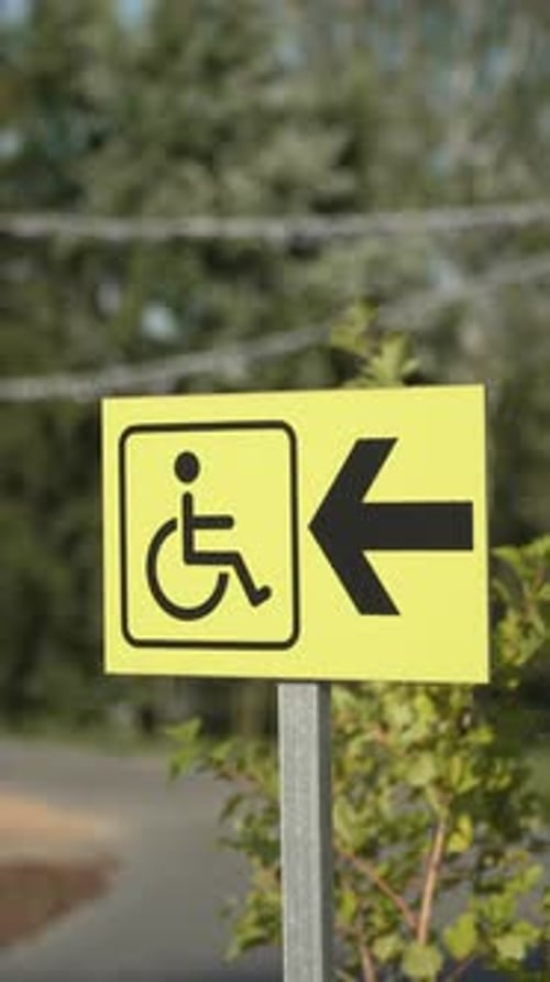Sign with Arrow and Wheelchair Pictogram in Park for People with Disabilities
