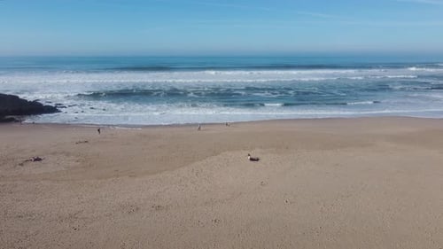 Drone shot flying over a beach on a beautiful morning with a few people walking around.