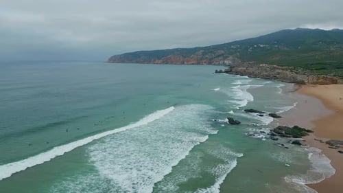 Ocean Waves Crashing Shore Cloudy Day Aerial View Rugged Cliffs Over Surfers