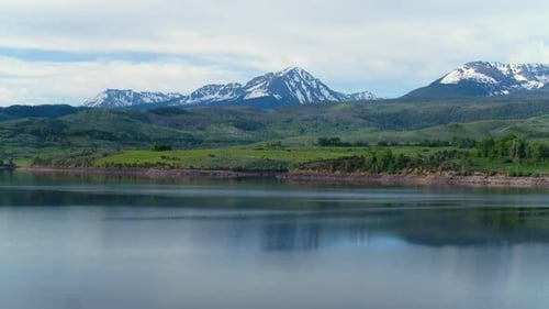 Aerial Drone of Lake in Colorado Rocky Mountains with Forest Trees and Snow-Capped Peaks in the Dist
