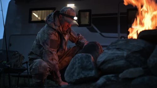 Un chasseur vêtu d'un revêtement de camouflage brûle un feu de camp à côté de son camping-car