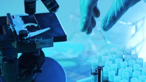 Hand Selecting Blood Sample Next to Microscope