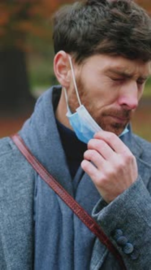 Person Carefully Adjusting Protective Face Covering Amidst Autumn Park Scenery During Health