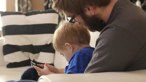 Child Using Tablet with Man on Couch