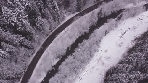 Aerial Directly Over a Remote Road Winding Through a Valley a Flowing Stream a Winter Landscape