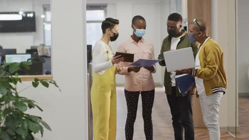 Diverse group of male and female business colleagues wearing face masks, working in office