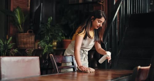 Woman, waitress or cleaning table with spray bottle for hospitality, hygiene or sanitation in cafe