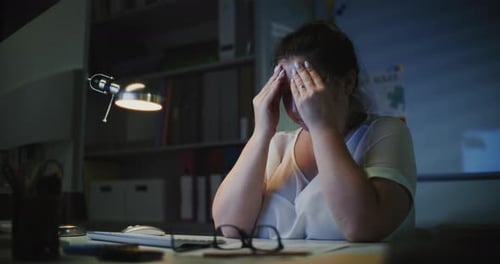 Exhausted Female Teacher Sitting at Computer in Empty Classroom Late at Night