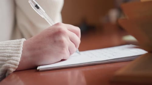 Close Up Hand Writing on Notebook Beside Open Book with Soft Background Blur