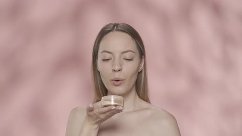 Beautiful Seminude Woman with a Jar of Powder in Her Hands in the Studio on a Pink Background Close