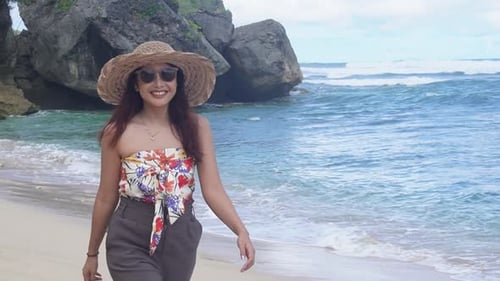 Slow motion side view of Asian woman wearing tube top walking by beach at noon - Female tourist on s