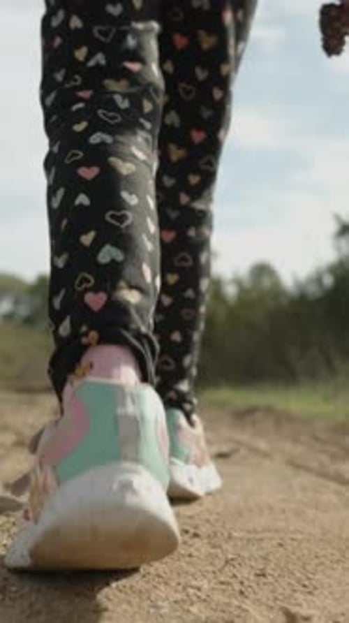 Vertical video. View from Below on the Legs of a Little Girl Walking on a Sandy Path in the Forest.