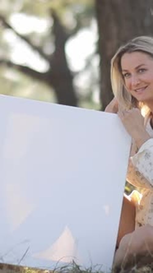 Blonde Woman Holds Blank Sign Outdoors in Nature