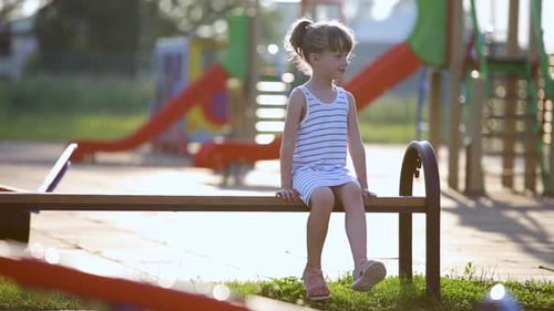 Cute Child Girl Waiting for Her Mother Sitting on a Bench on Summer Playground in Kindergarten Yard