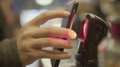 Un hombre sostiene su teléfono inteligente frente a un lector de códigos de barras de la caja registradora para pagar la cuenta y usa la l