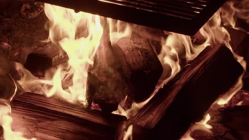 Close up camp fire logs burn hot orange at night, cooking grill on top