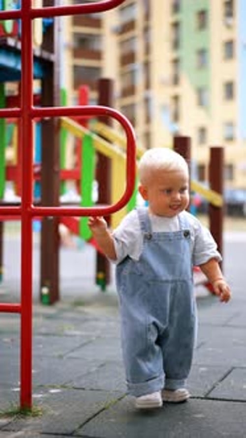 Adorable Caucasian child in jeans romper runs by the playground. Happy kid at the walk outdoors.