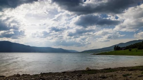 See mit klarem Wasser und Steinufer im Fichtenwald mit Tannen vor einem Tageshimmel