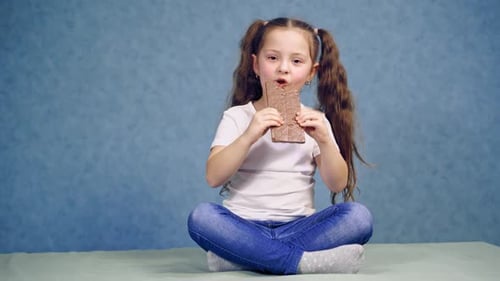 Girl eating chocolate bar. Girl sitting on the table and eating chocolate