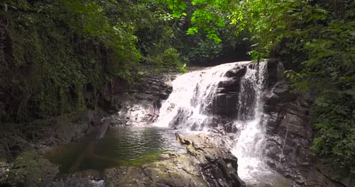 A spectacular waterfall surrounded by lush vegetation. Aerial drone shot, tracking panning slow moti
