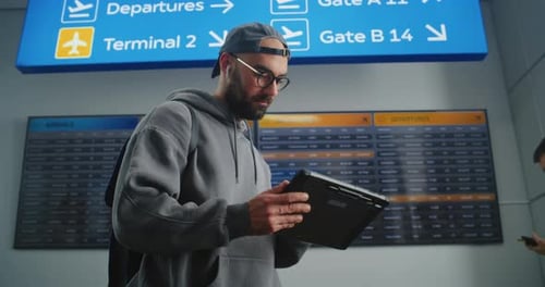 Traveler Uses Tablet at Airport Flight Board