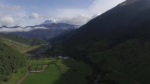 Luftflug durch das grüne Tal mit einem schneebedeckten Berg in der Ferne