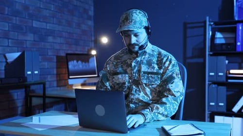 Military service. Soldier in headset working at wooden desk in office at night
