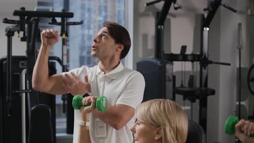Coach Instructing Fit Woman Doing Exercise with Light Dumbbells in Gym