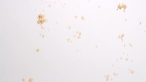 Brown sugar clumps falling in slow motion on white studio backdrop in 4k