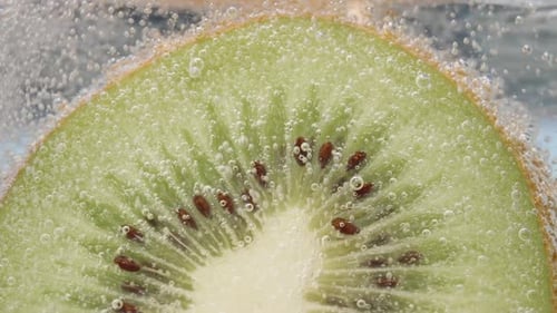 Half a kiwi in a glass of soda. Bubbles slowly rise up, macro