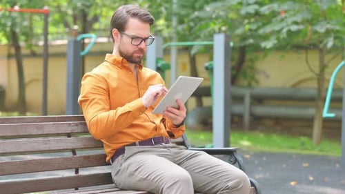 Middle Aged Man Using Digital Tablet while Sitting on Bench