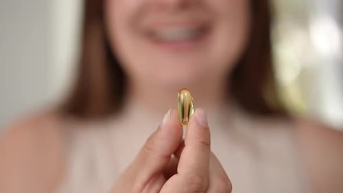Woman Holds a Golden Vitamin Capsule Close Up