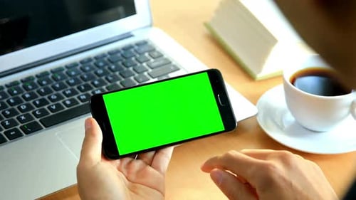 Man Taps Green Screen Phone at Wooden Desk