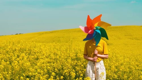 Caucasian woman in a yellow shirt and white pants in a rapeseed field with pinwheel, Poland