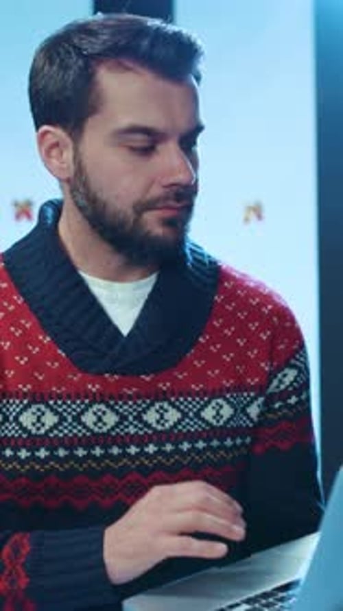 A Festive Man with Laptop in a Stylish Sweater Enjoying the Holiday Spirit and Cheer