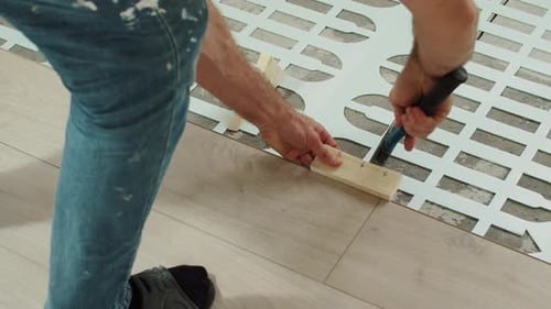 Worker Securing Decorative Flooring with Hammer and Spacer