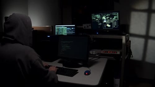 Hacker in Hoodie Entering Code on Computer Screen