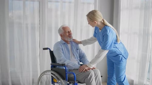 Nurse Comforts Senior Man in Wheelchair Indoors