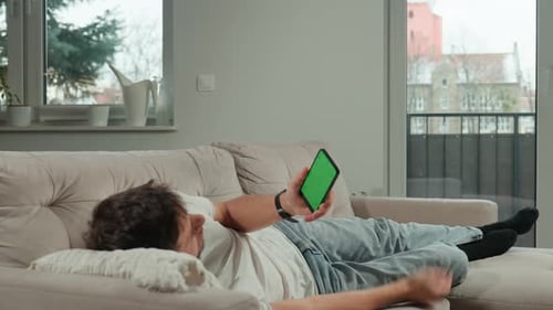 Man Relaxing on Sofa Using Smartphone with Green Screen