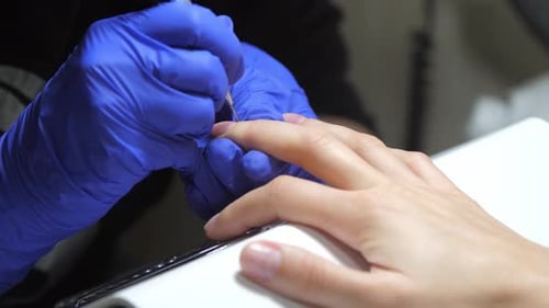 Process of making manicure. Closeup of manicurist in blue gloves applying base coat on client femal