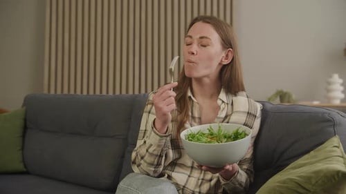 Woman Eats Healthy Salad on Gray Sofa