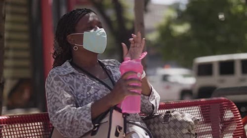 Mature woman removes facemask for refreshing water break in sunny city park
