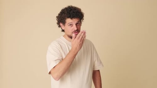 Happy man looking at camera sends air kisses in studio on beige background