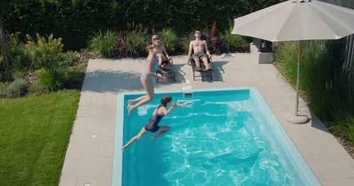 Children Jump Into the Pool Slow Motion Video Adults Rest on Sun Loungers Nearby