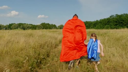 Back View of Cute Little Girl and Father Playing in Superhero on Green Field