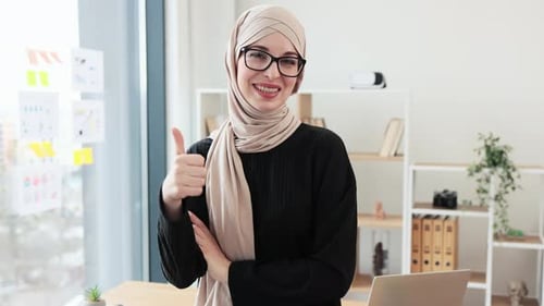 Smiling Woman in Headscarf Gives Thumbs Up in Office