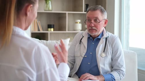 Senior Man Doctor Examining Yound Woman in Doctor Office or at Home