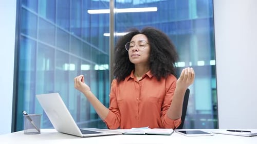 Young african american businesswoman meditates with her eyes closed sitting at workplace in office.